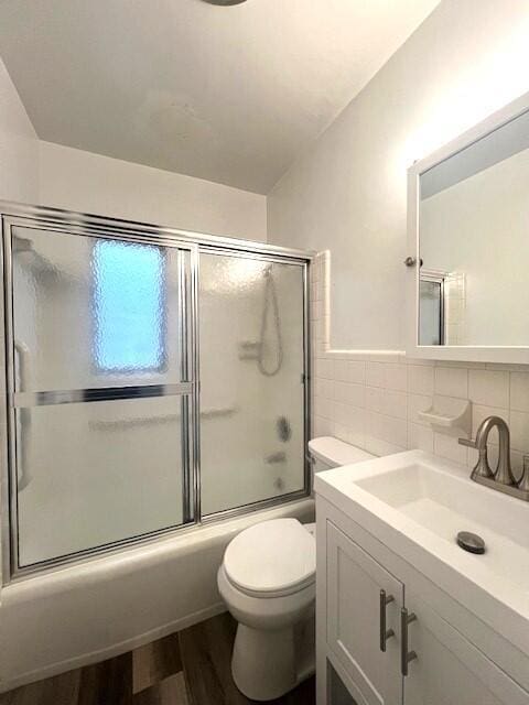 full bathroom featuring enclosed tub / shower combo, wood-type flooring, toilet, vanity, and tile walls