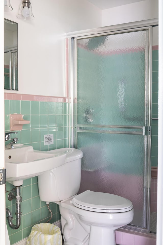 bathroom featuring a shower with door, toilet, and tile walls