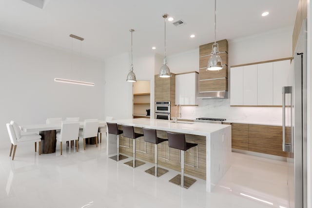 kitchen with hanging light fixtures, white cabinets, a kitchen island with sink, and a kitchen breakfast bar