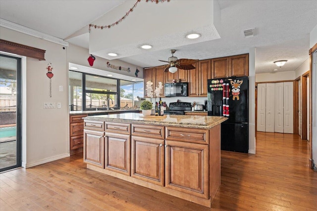 kitchen featuring light stone counters, a textured ceiling, ceiling fan, black appliances, and a kitchen island