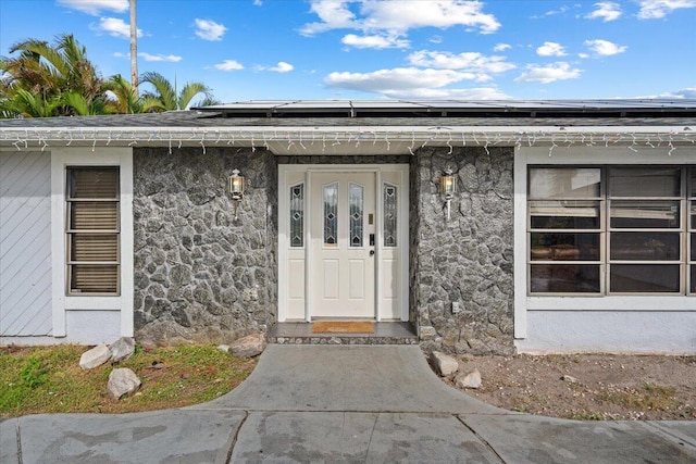 entrance to property featuring stone siding, stucco siding, and solar panels