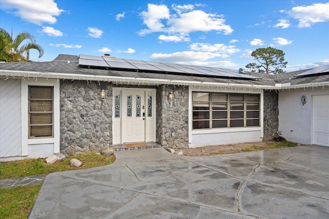 doorway to property featuring solar panels, concrete driveway, stone siding, and stucco siding