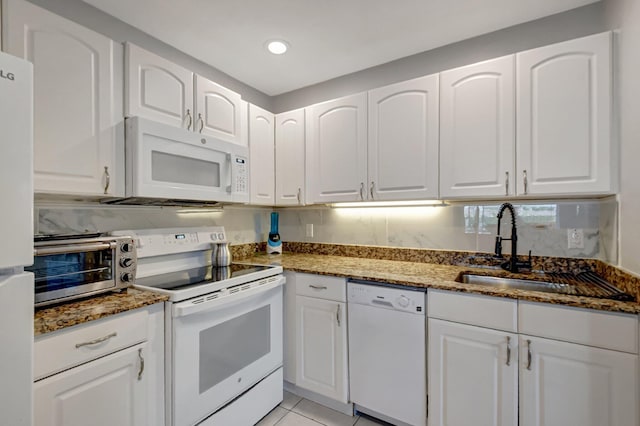 kitchen featuring dark stone counters, white appliances, sink, light tile patterned floors, and white cabinets