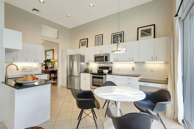 kitchen featuring white cabinets, backsplash, a towering ceiling, and stainless steel appliances