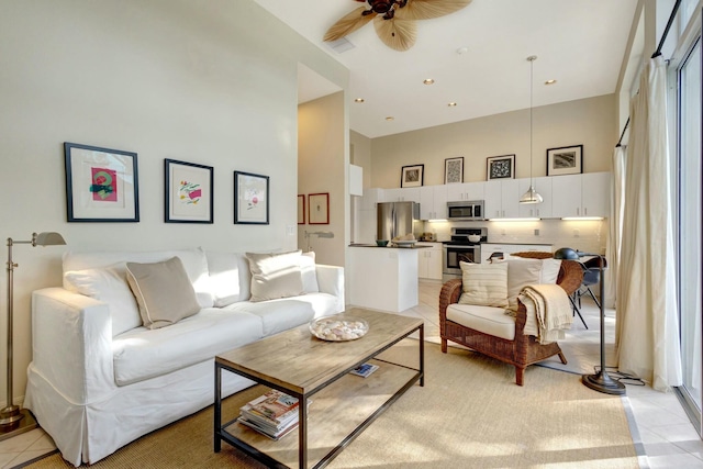 tiled living room with ceiling fan, plenty of natural light, and a towering ceiling