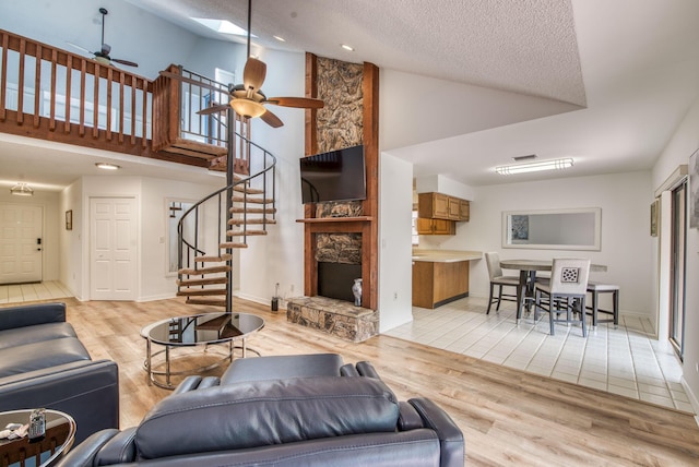 living room featuring high vaulted ceiling, a skylight, ceiling fan, a textured ceiling, and light hardwood / wood-style floors