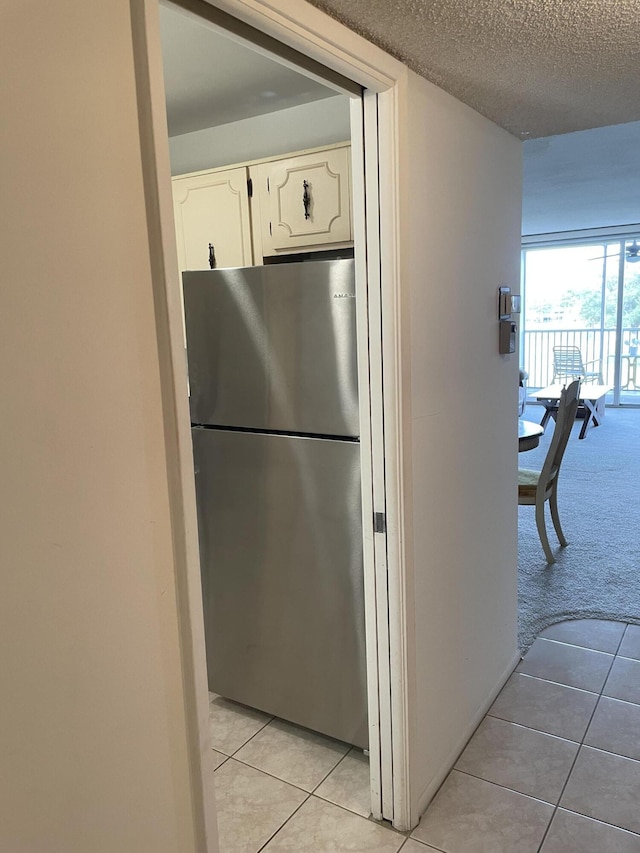 kitchen with stainless steel refrigerator, white cabinets, light colored carpet, and a textured ceiling