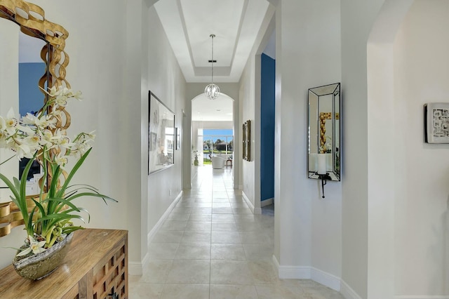 hall with a tray ceiling and light tile patterned floors