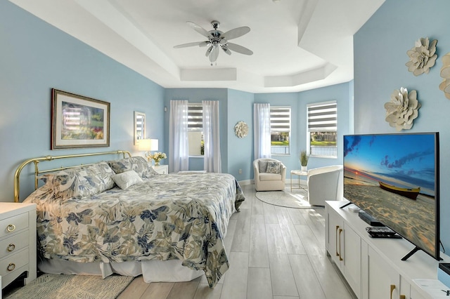 bedroom with ceiling fan, a raised ceiling, and light hardwood / wood-style flooring