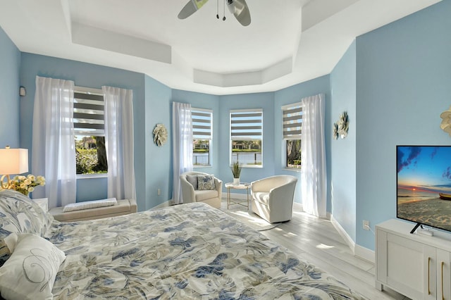 bedroom with ceiling fan, light wood-type flooring, and a tray ceiling