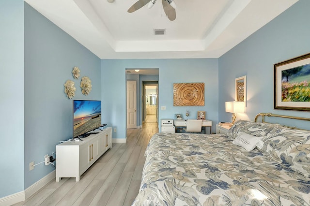 bedroom with a tray ceiling, ceiling fan, and light hardwood / wood-style flooring