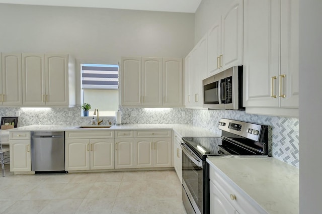 kitchen featuring sink, decorative backsplash, light tile patterned floors, appliances with stainless steel finishes, and white cabinetry