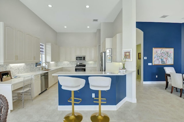 kitchen featuring appliances with stainless steel finishes, tasteful backsplash, a breakfast bar, sink, and white cabinetry