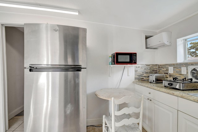 kitchen featuring light stone counters, freestanding refrigerator, white cabinetry, backsplash, and a wall mounted AC