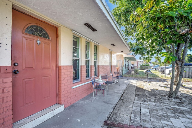 entrance to property featuring brick siding, fence, and stucco siding