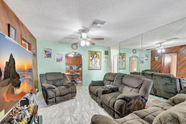 living room with ceiling fan, a textured ceiling, and wood walls