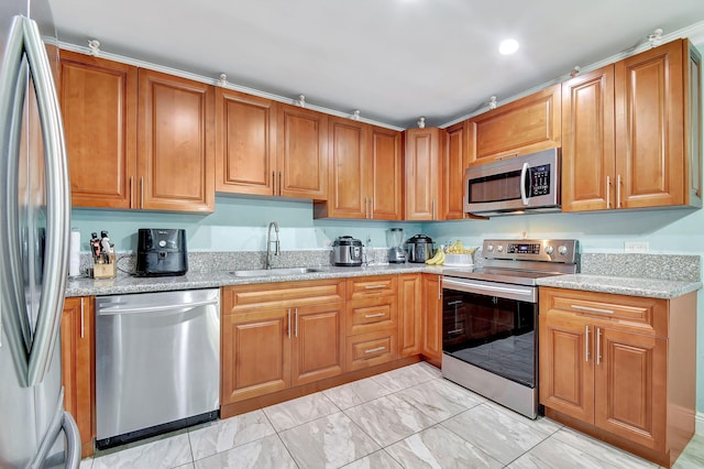 kitchen featuring light stone counters, appliances with stainless steel finishes, brown cabinets, and a sink