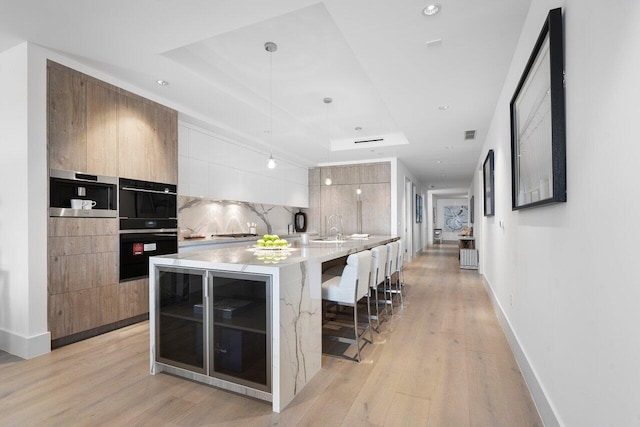 kitchen with an island with sink, tasteful backsplash, decorative light fixtures, a kitchen breakfast bar, and light hardwood / wood-style flooring