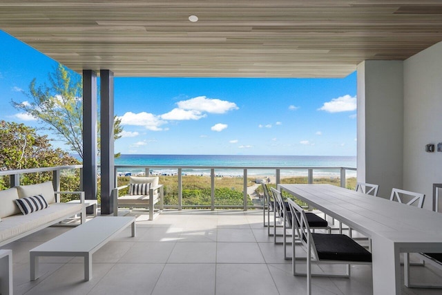 balcony with an outdoor living space, a water view, and a view of the beach