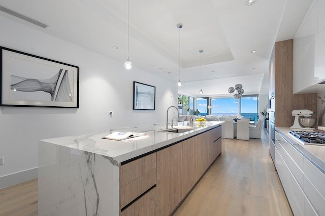 kitchen featuring a spacious island, sink, a tray ceiling, hanging light fixtures, and light stone counters