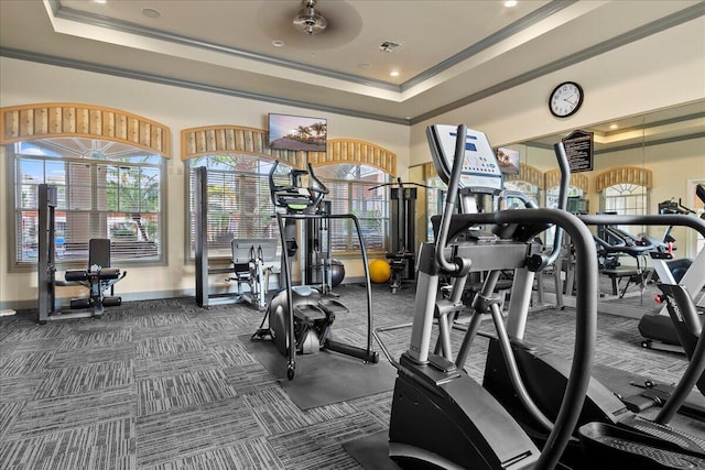 gym featuring ceiling fan, dark carpet, ornamental molding, and a tray ceiling