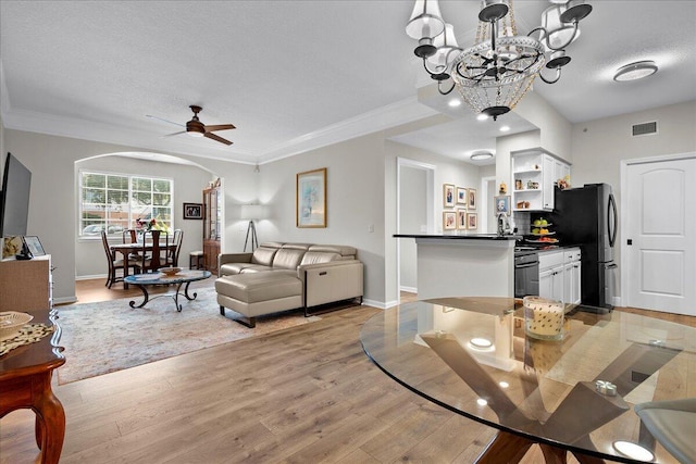 living room with a textured ceiling, ceiling fan with notable chandelier, crown molding, sink, and light hardwood / wood-style floors