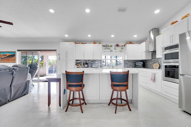 kitchen featuring a kitchen bar, white cabinets, and wall chimney exhaust hood