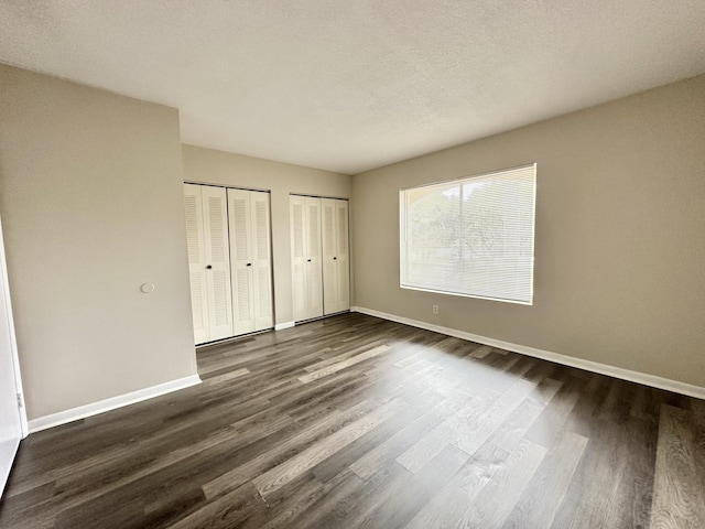 unfurnished bedroom featuring dark hardwood / wood-style floors, a textured ceiling, and multiple closets