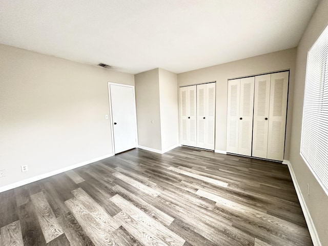 unfurnished bedroom featuring dark wood-type flooring and two closets