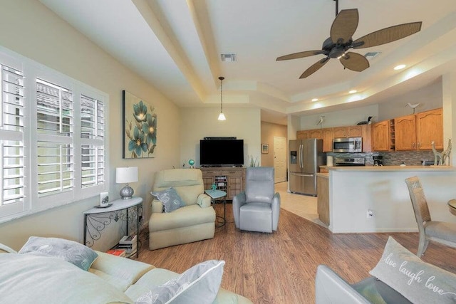 living room featuring a raised ceiling, ceiling fan, and light wood-type flooring