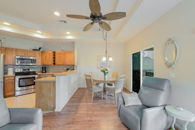 kitchen featuring hanging light fixtures, decorative backsplash, light hardwood / wood-style floors, kitchen peninsula, and stainless steel appliances