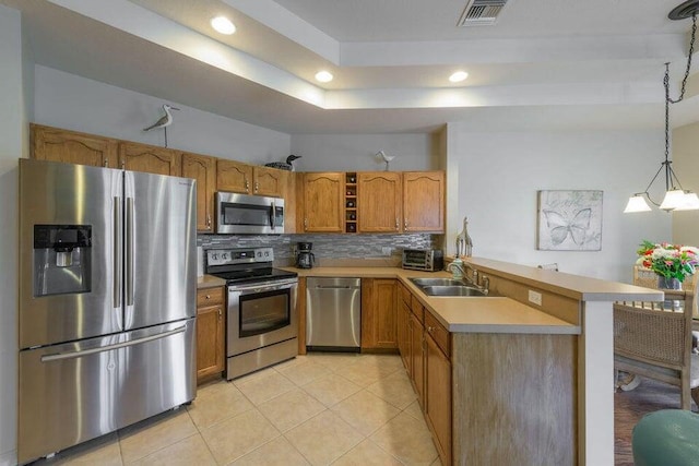 kitchen featuring kitchen peninsula, tasteful backsplash, stainless steel appliances, sink, and hanging light fixtures