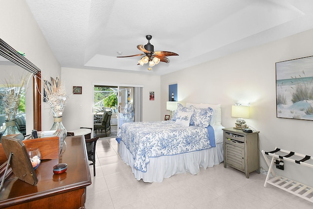 bedroom with a textured ceiling, light tile patterned floors, access to outside, a tray ceiling, and ceiling fan