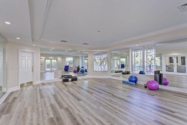 exercise area with french doors, light wood-type flooring, a tray ceiling, and ornamental molding