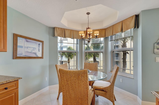 dining space with a tray ceiling, an inviting chandelier, and light tile patterned flooring