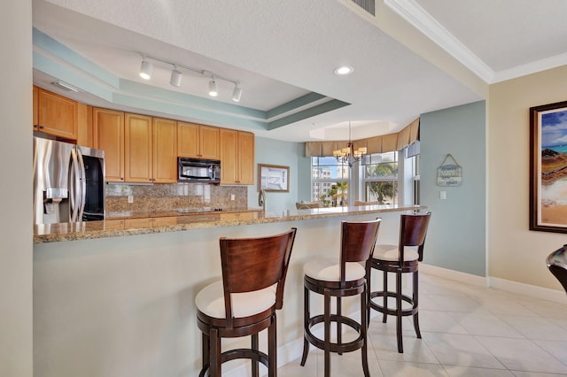 kitchen with a raised ceiling, light stone counters, backsplash, kitchen peninsula, and stainless steel fridge