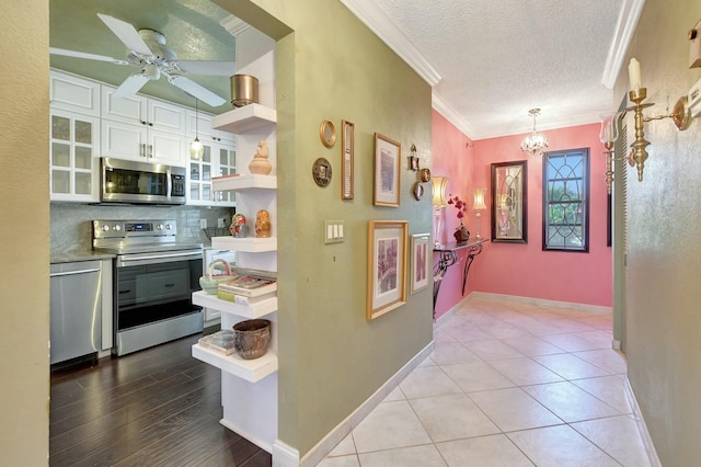 kitchen featuring white cabinetry, pendant lighting, a textured ceiling, appliances with stainless steel finishes, and ornamental molding