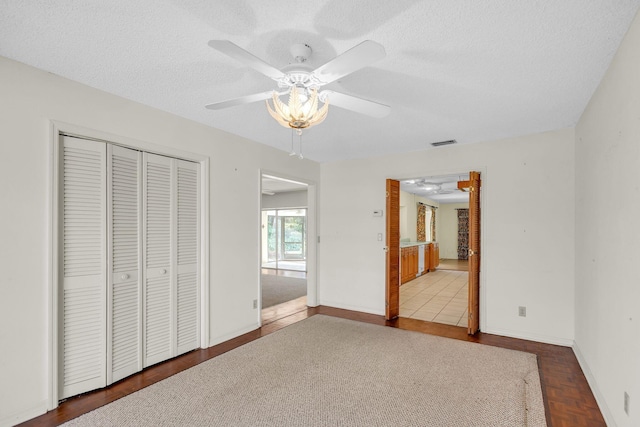 unfurnished bedroom with wood-type flooring, a textured ceiling, a closet, and ceiling fan