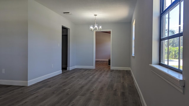 empty room with dark wood-type flooring and a notable chandelier