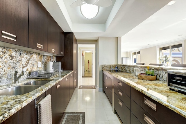 kitchen featuring tasteful backsplash, light stone counters, dark brown cabinets, a tray ceiling, and sink