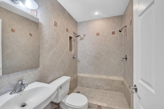 bathroom featuring toilet, a tile shower, sink, and tile walls