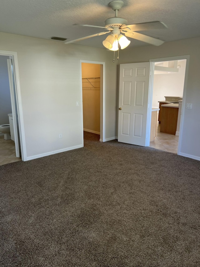 unfurnished bedroom featuring a walk in closet, connected bathroom, light carpet, and a textured ceiling