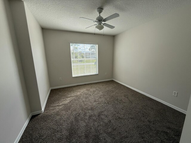 empty room featuring dark colored carpet, ceiling fan, and a textured ceiling