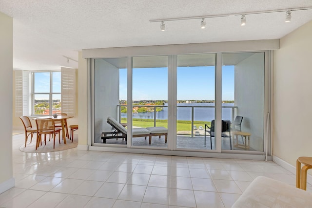 doorway to outside with a water view, light tile patterned floors, and a textured ceiling