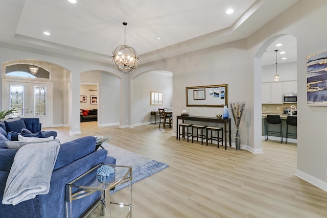 living room with french doors, plenty of natural light, a chandelier, a tray ceiling, and light wood-type flooring