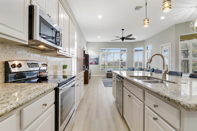 kitchen featuring sink, light wood-type flooring, decorative light fixtures, white cabinetry, and stainless steel appliances