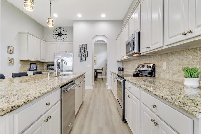 kitchen with white cabinets, sink, appliances with stainless steel finishes, decorative light fixtures, and light stone counters