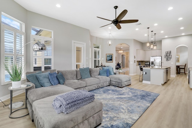 living room featuring ceiling fan with notable chandelier and light wood-type flooring