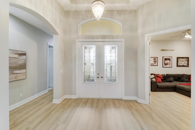 entrance foyer featuring french doors, a towering ceiling, ceiling fan with notable chandelier, and light wood-type flooring