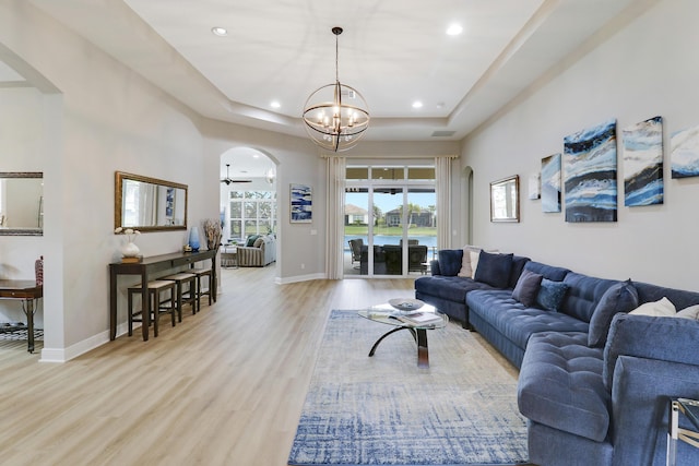 living room featuring ceiling fan with notable chandelier, light hardwood / wood-style floors, and a raised ceiling